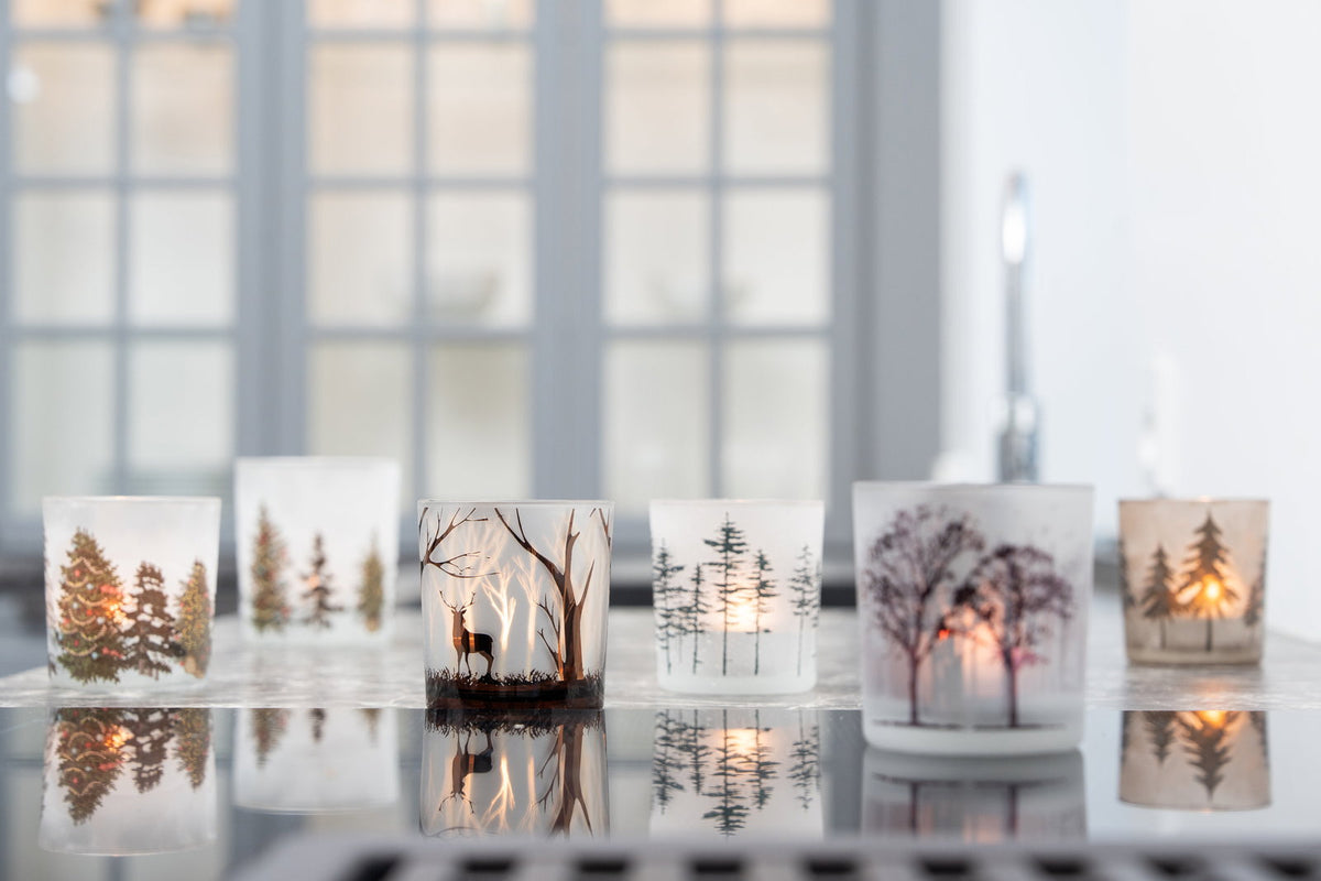 Fyrfadsglas med vintermotiver og tændte lys i vindueskarm